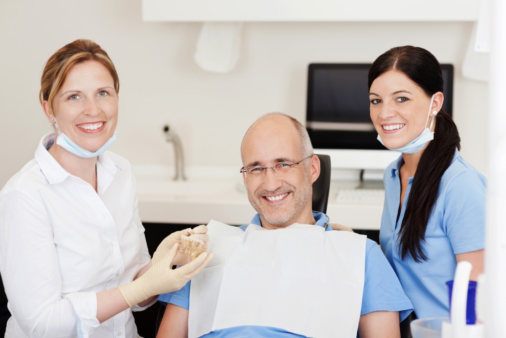 A smiling patient with a dentis on one side of him and a hygenist on the other